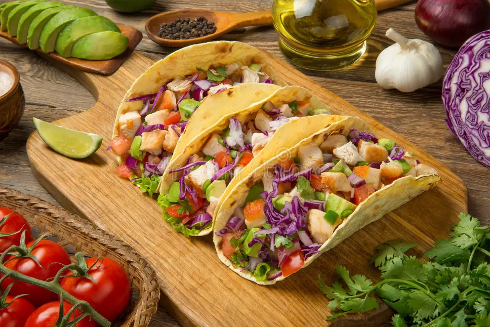 Chicken tacos with fresh salsa, avocado, and lime wedges on a rustic wooden table.